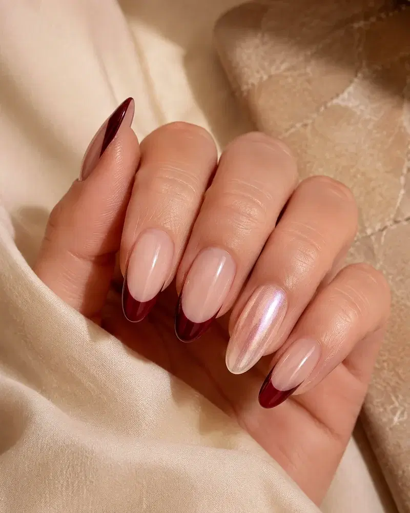Een afgewerkte set lange amandelvormige gelverlengingen met bordeauxrode French tips en een parelmoeren accentnagel.